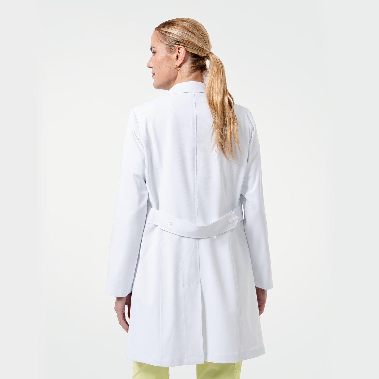 Image of Model wearing a white medical lab coat over yellow scrubs, shown from the back to highlight the coat’s back vent and belt detail on a white background.