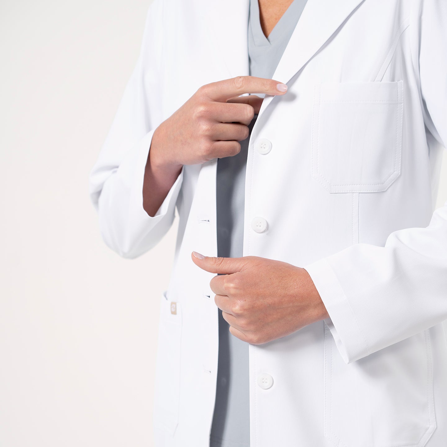 Image of Close-up of the Women’s Long Lab Coat LCW-04 in white, focusing on the chest pocket and front buttons as the model adjusts the coat.
