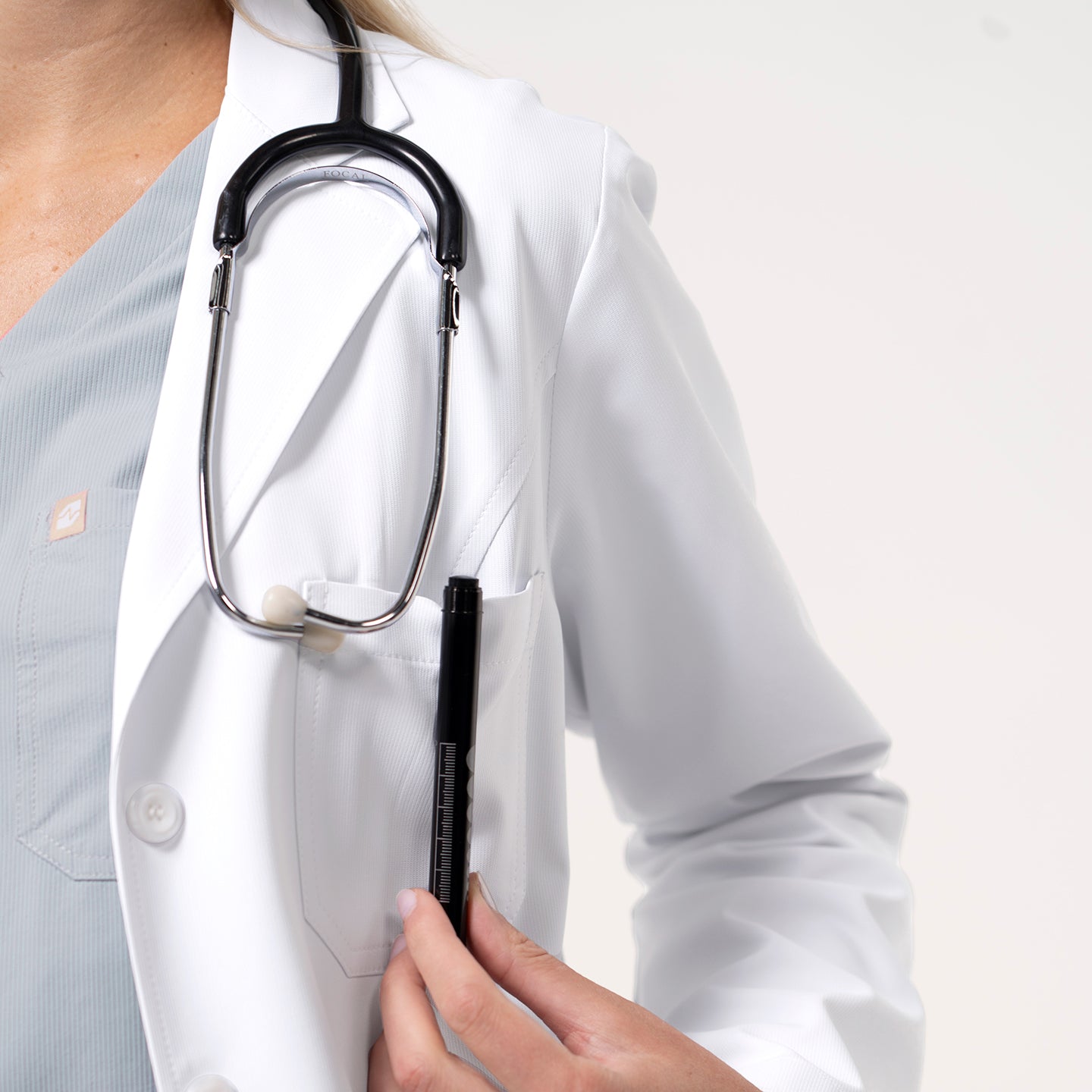 Image of Women’s Long Lab Coat LCW-04 in white, showing the chest pocket holding a pen while the model wears a stethoscope around the neck.
