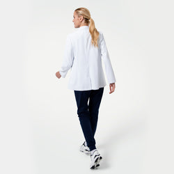 Image of Back view of the Women’s Short Lab Coat LCW-02 in white, showing the model walking away with the coat’s straight hemline and side vents visible, paired with navy scrub pants and white sneakers.