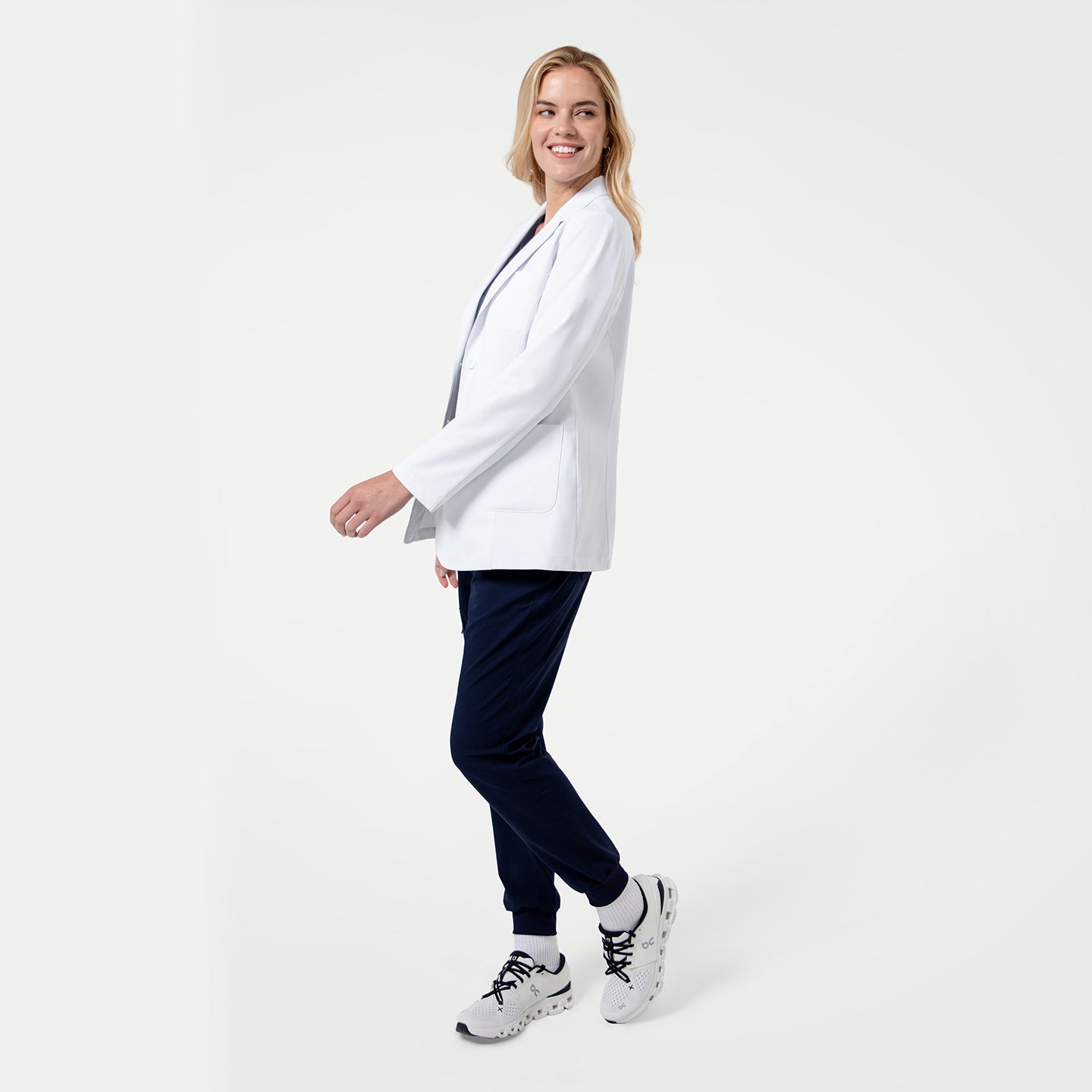 Image of Woman wearing a white lab coat, navy pants, and white sneakers on a white background