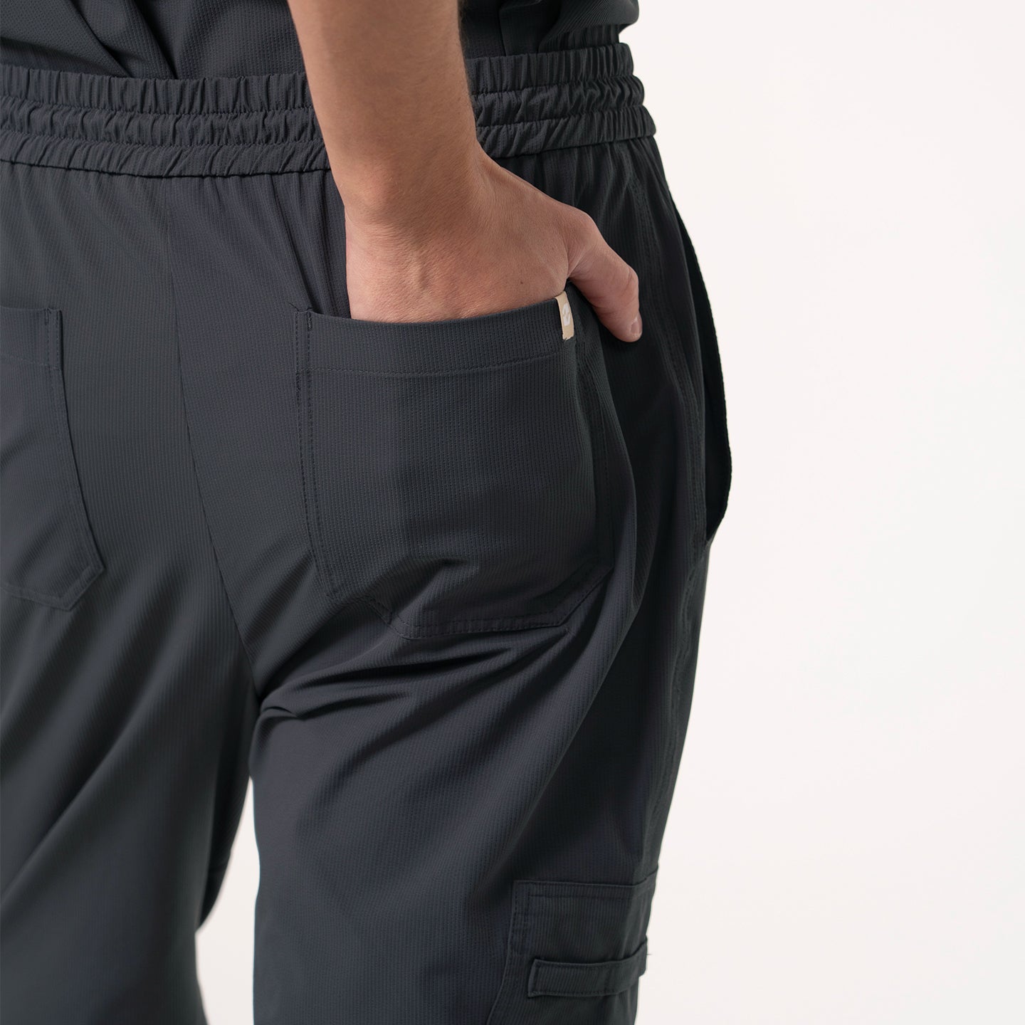 Back view of Deep Gray Zipper Pocket Jogger Scrub Pants, showing the right hand placed inside the back pocket with visible elastic waistband and additional pocket stitching detail.