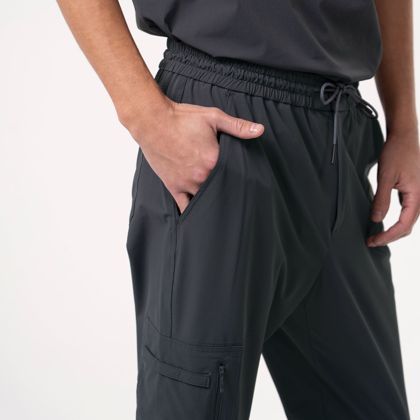 Image of Close-up of Deep Gray Zipper Pocket Jogger Scrub Pants, showing the left hand placed in the side pocket with an elastic waistband and visible pocket detail.