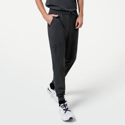 Image of Male model in mid-step with one hand in his pocket, showcasing Zipper Pocket Jogger Scrub Pants in Deep Gray paired with a matching scrub top and white sneakers.