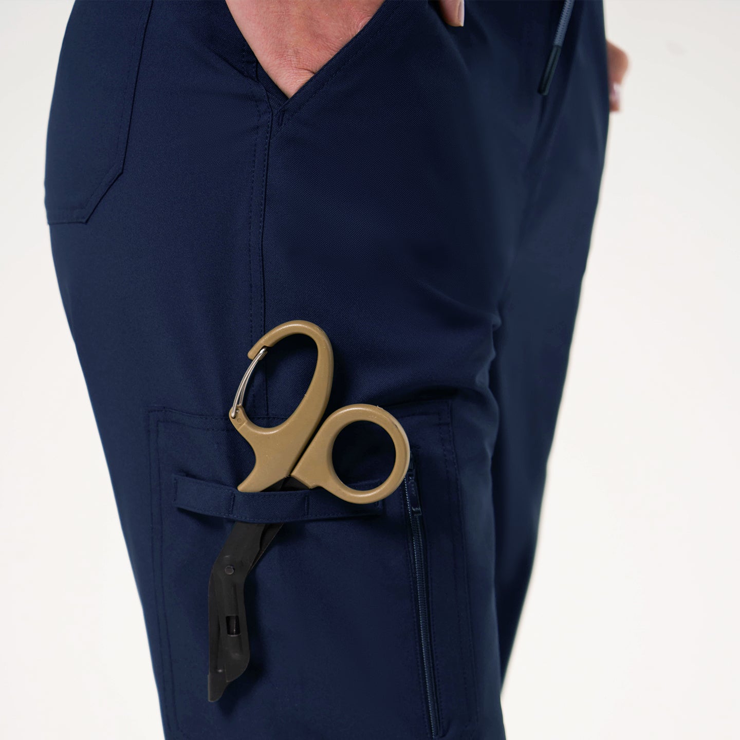 Image of Close-up of navy jogger scrub pants with a side zipper pocket holding a pair of medical shears.