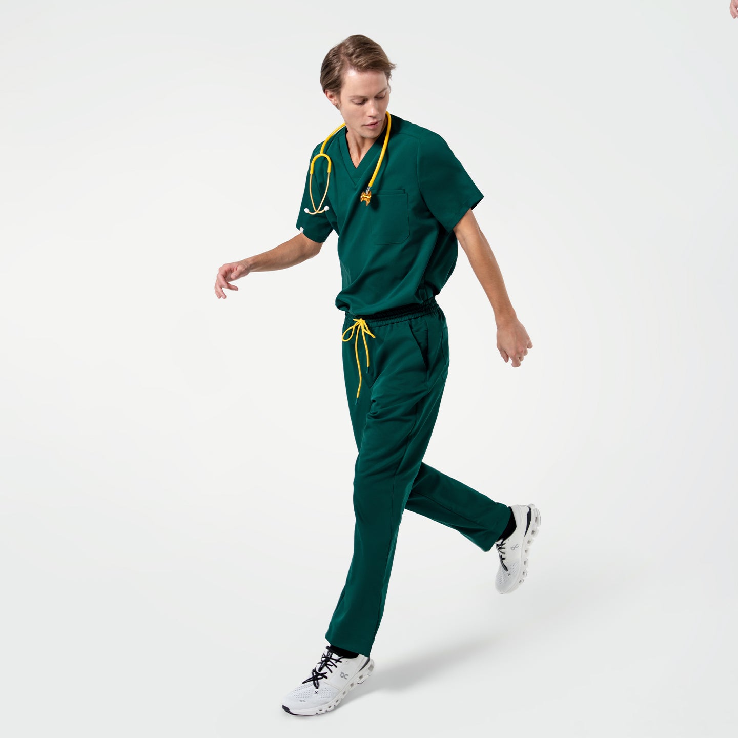 Image of In Pine Green zipper pocket scrub pants, the individual moves with one leg forward and the other leg behind, arms in motion.